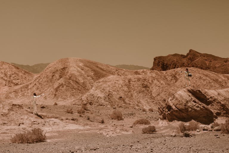 Two astronauts in a rocky desert landscape, evoking Mars exploration.